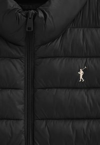 Svart puffjacka med hög krage, vertikal quilt-design och dragkedja. Anmärkningsbar liten logotyp broderad i beige.