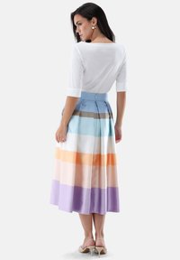 Langer, plissierter Rock mit horizontalen pastellfarbenen Streifen in Blau, Orange und Lila, kombiniert mit einem weißen Oberteil mit dreiviertellangen Ärmeln.