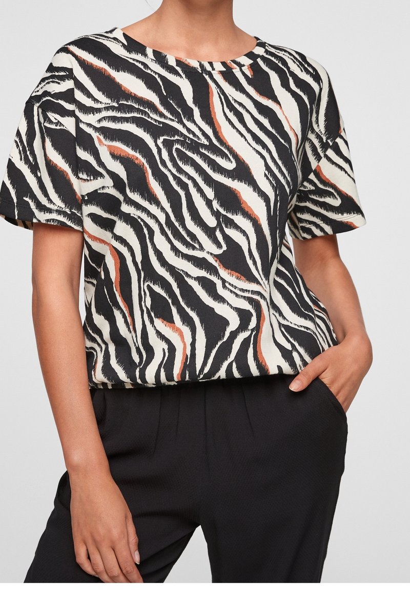 Blusa de manga corta en patrón de rayas de cebra en negro y crema con acentos naranjas, con cuello redondo y ajuste relajado.