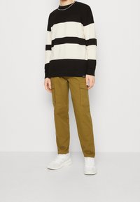 Jersey de rayas negras y crema, material de algodón; combinado con pantalones cargo verde oliva con dos bolsillos laterales; zapatillas blancas completan el conjunto.