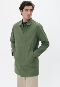 Chaqueta impermeable verde con un diseño aerodinámico, mangas largas y bolsillos. Cuenta con un cuello y una textura suave.
