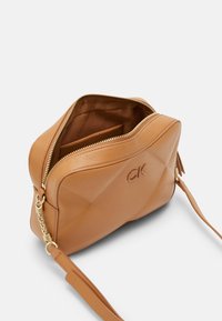 Brązowa torebka ze skóry z geometrycznym wzorem, złotymi okuciami i zamkiem błyskawicznym. Wnętrze wyposażone w kontrastową podszewkę oraz małą kieszonkę.