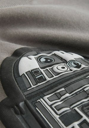 R2-D2-Grafik auf einem grauen Stoff gedruckt, mit schwarz-weißen Details, strukturiertem Oberfläche und ausgeprägten runden und rechteckigen Formen.