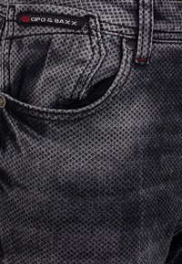 Schwarz und grau gemusterte Jeans aus Denim mit einer Vordertasche mit kontrastierenden Nähten, Markenzeichen und Metallknopf-Details.
