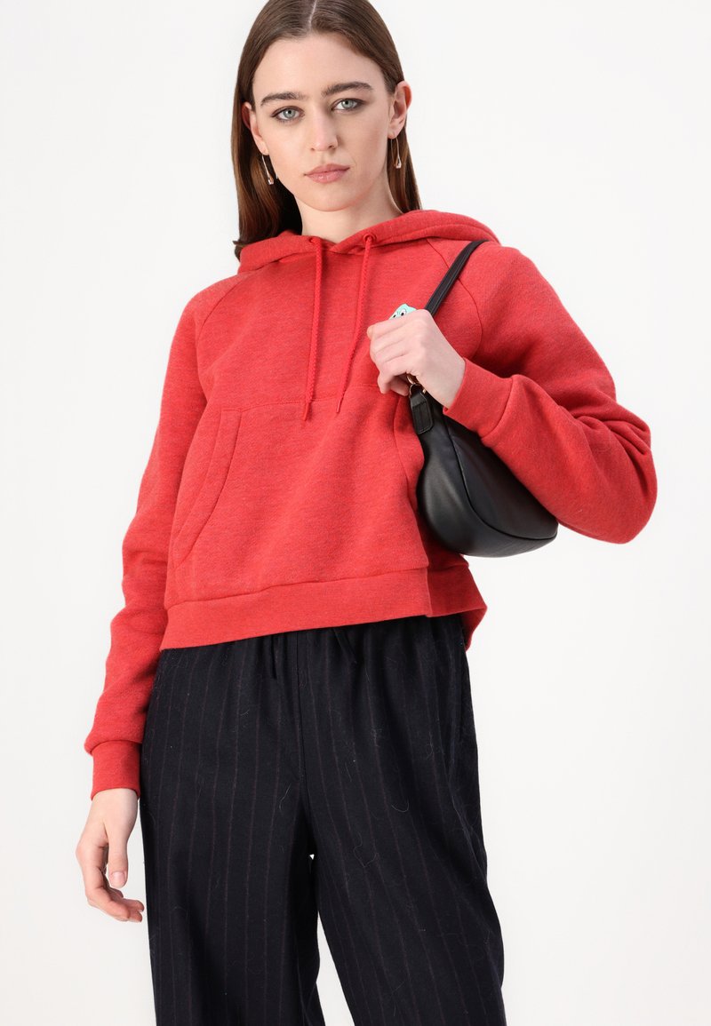 Hoodie rouge court avec une poche avant et des cordons de serrage réglables, associé à un pantalon large à rayures noires. Accessoire sac à main noir.