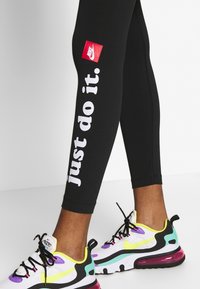 Svarta tights med "just do it." i vit text, med en röd Nike-logotyp. Bärs med färgglada Nike-sneakers med en genomskinlig luftsole.