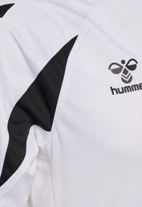Weißes Sporttrikot mit schwarzen geometrischen Einsätzen unter dem Arm und schwarzem "hummel" Markenlogo mit Bienen-Symbol auf der Brust.