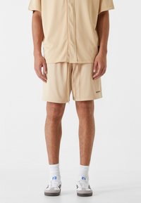 Ensemble en beige composé d'une chemise à manches courtes en maille et d'un short, avec une coupe décontractée, une taille à cordon de serrage et un petit logo sur le short.