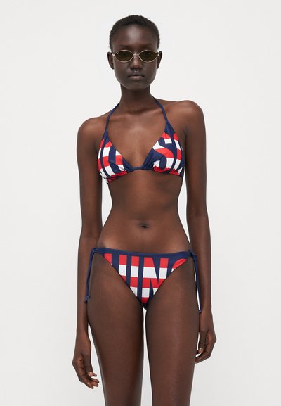 Dviejų dalių bikinis, kuriame yra trikampis halterio tipo viršus ir šoninės raištelių konstrukcijos kelnaitės. Medžiaga tamsiai mėlyna su raudonais ir baltais grafikos užrašais.