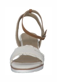 Sandale compensée en tissu blanc avec des sangles effilochées et une bride de cheville en cuir marron, présentant un léger talon et une semelle intérieure rembourrée.