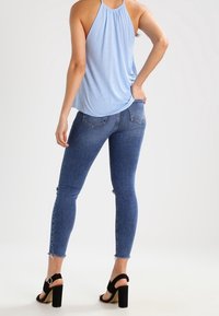 Haut dos nu bleu clair à coupe décontractée, associé à un jean skinny délavé foncé avec ourlet effiloché et deux poches arrière. Sandales à talons blocs noires.