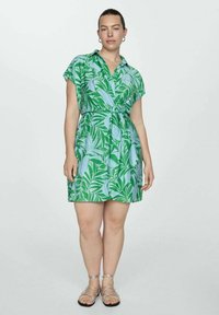 Rochie cu maneci scurte în verde și albastru deschis, cu model de frunze, talie strânsă și croi lejer. Sandale plate completează ținuta.