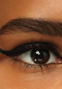 L'eyeliner liquido è applicato lungo la palpebra superiore, creando una linea nera audace. Il primo piano mette in risalto la pelle liscia, le ciglia scure e l'occhio lucido.