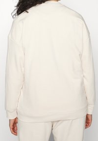 Lichtbeige sweatshirt met een ontspannen pasvorm, ronde hals en geribbelde manchetten. Gemaakt van zacht materiaal, met een effen textuur zonder patronen.