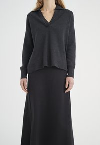 Tmavě šedý pletený svetr s výstřihem do V a límcem, spárovaný s dlouhou černou sukní. Materiály se zdají být měkké a pohodlné.