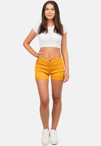 Gele denimshorts met een fitted ontwerp, knoopsluiting en voorzakken, gecombineerd met een witte korte mouwen crop top en witte sneakers.