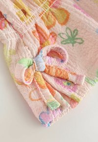 Primer plano de tela rosa con estampado floral multicolor y un pequeño lazo de tela atado en el puño elástico fruncido.