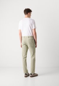 Vaaleanvihreät chinosit, jotka on valmistettu puuvillasta, slim fit -malliset, sivu- ja takataskut, sekä ruskeat tennarit mustilla yksityiskohdilla. Yksinkertainen valkoinen t-paita.
