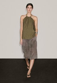 Zelená halter top z lehkého materiálu se skládáním na výstřihu, spárovaná se šedou semišovou sukní po kolena s jemnou texturou.