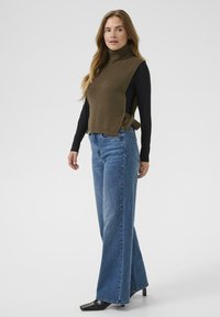 Olivengrøn, ribbet turtleneck sweater lagdelt over en sort bluse med lange ærmer, kombineret med lyseblå, flagrende jeans og sorte spidse hæle.