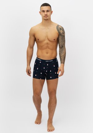 Boxers bleu marine avec un motif festif de bonhommes de neige et de rennes ; ceinture élastique avec le logo "HAPPY SHORTS" ; matériau en coton.