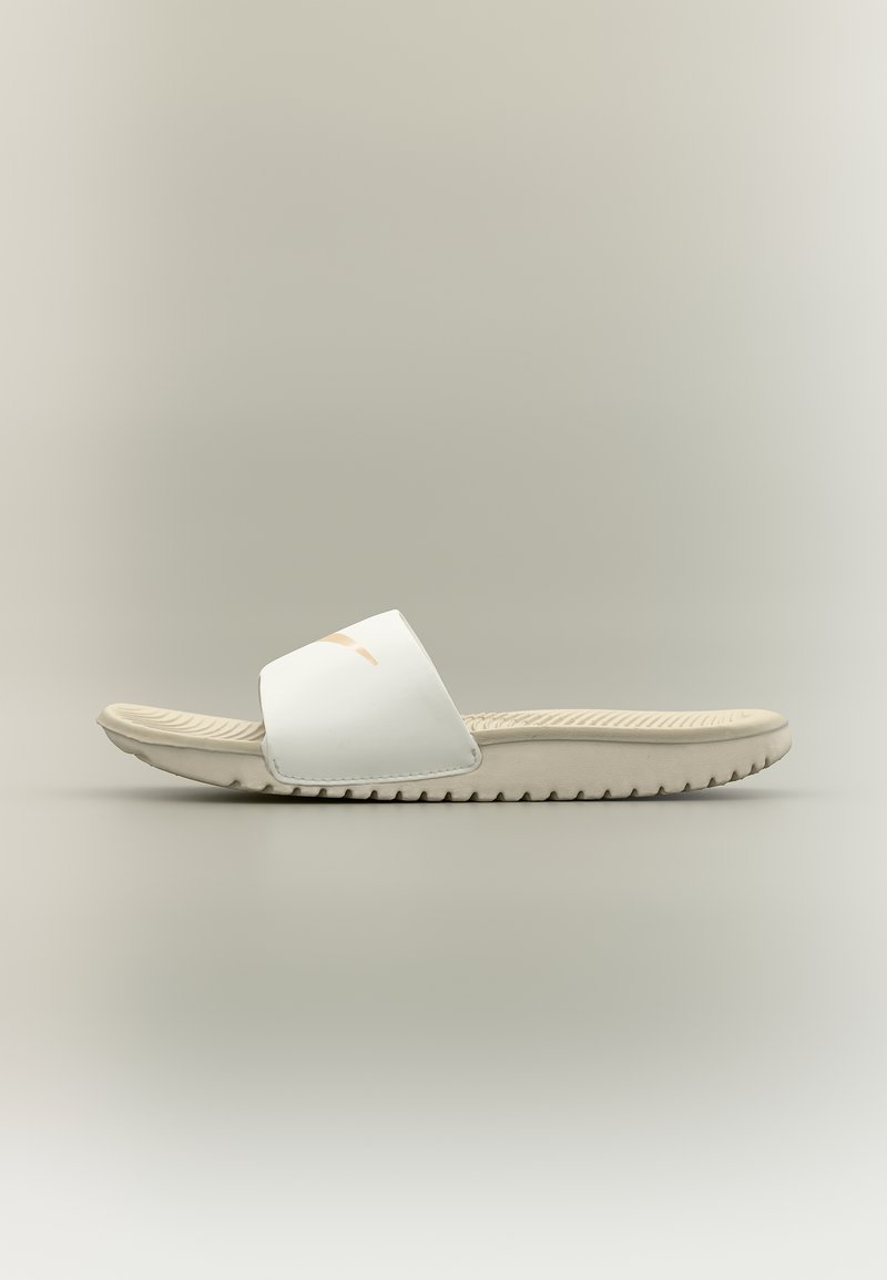 Πλευρική όψη ενός μπεζ σανδαλιού τύπου slide της Nike με υφή στη σόλα και λευκό λουράκι που φέρει ένα μπεζ λογότυπο Nike.