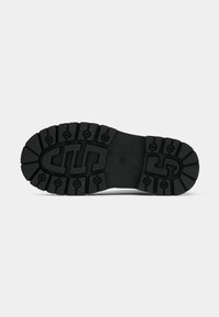 Suela de goma negra con un patrón de surcos profundos, que presenta indentaciones circulares y rectangulares, proporcionando tracción y durabilidad.
