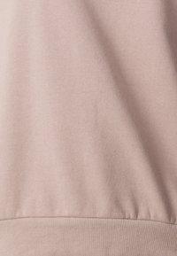 Tessuto di felpa rosa chiaro con una consistenza morbida, caratterizzato da un orlo a coste nella parte inferiore e senza motivi o dettagli hardware visibili.