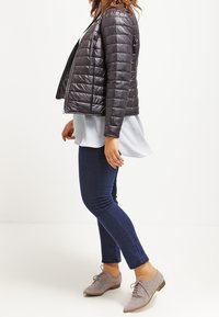 Sort, quiltet pufferjakke med en tætsiddende pasform, parret med en lyseblå bluse, mørke jeans og grå snørebåndssko.