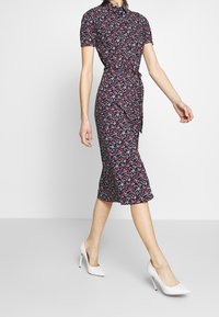 Blommig klänning med krage, korta ärmar och knytmidja. Mörk bakgrund med små röda och vita blommor. Midilängd.