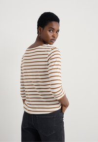 Gestreepte lange mouwen top in crème en bruin, met een bateauhals en driekwart mouwen, gemaakt van een zachte, lichte stof.