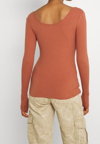 Langärmliges Rippenshirt in Terrakotta mit weitem Rundrücken und taillierter Silhouette, kombiniert mit cremefarbenen gemusterten Cargo-Hosen.