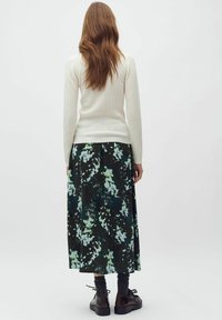 Krémový žebrovaný top s dlouhým rukávem spojený s tmavou maxi sukní s květinovým potiskem v zelených a modrých odstínech. Černé boty s tkaničkami.