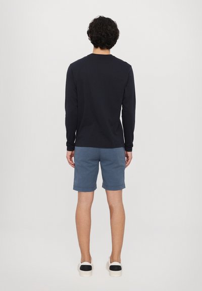 Camisa de manga larga navy combinada con pantalones cortos azul claro, con los puños enrollados. El modelo lleva zapatillas blancas con acentos negros.