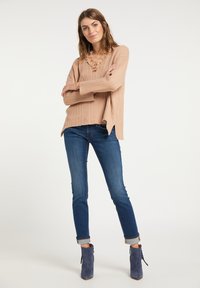Suéter de canalé rosa claro con escote en V y acentos de volantes, combinado con jeans ajustados azul oscuro y botas de tobillo azules.