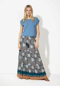 Blauw top met korte mouwen, gecombineerd met een lange rok met een patroon van bloemen in blauw, beige en bruin, met franjes.