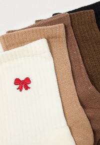 Cinque paia di calze: crema, marrone chiaro, marrone medio, marrone scuro e nero. La calza crema presenta un dettaglio di un fiocchetto ricamato rosso.