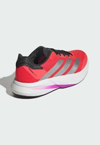 Red running shoe with black accents, silver stripes, and textured material. Features a white midsole with a purple detail. Lightweight design.