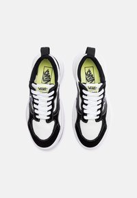 Scarpe da ginnastica in bianco e nero con una tomaia testurizzata, lacci bianchi e logo sulla linguetta. Presentano una suola spessa bianca e cuciture a contrasto.