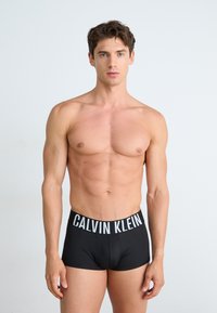 Zwarte boxershorts met een witte "CALVIN KLEIN" logo tailleband, soepel materiaal, aansluitend ontwerp en zonder zichtbare patronen of accenten.