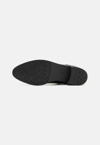 Suela de zapato negra con un acabado liso y una suela con patrón para un mejor agarre. Incluye marcas de tamaño y nombre de la marca.