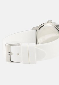 Witte siliconen horlogeband met zilveren gesp, gekruld om de achterkant van een zilveren horloge kast tegen een lichte achtergrond te tonen.