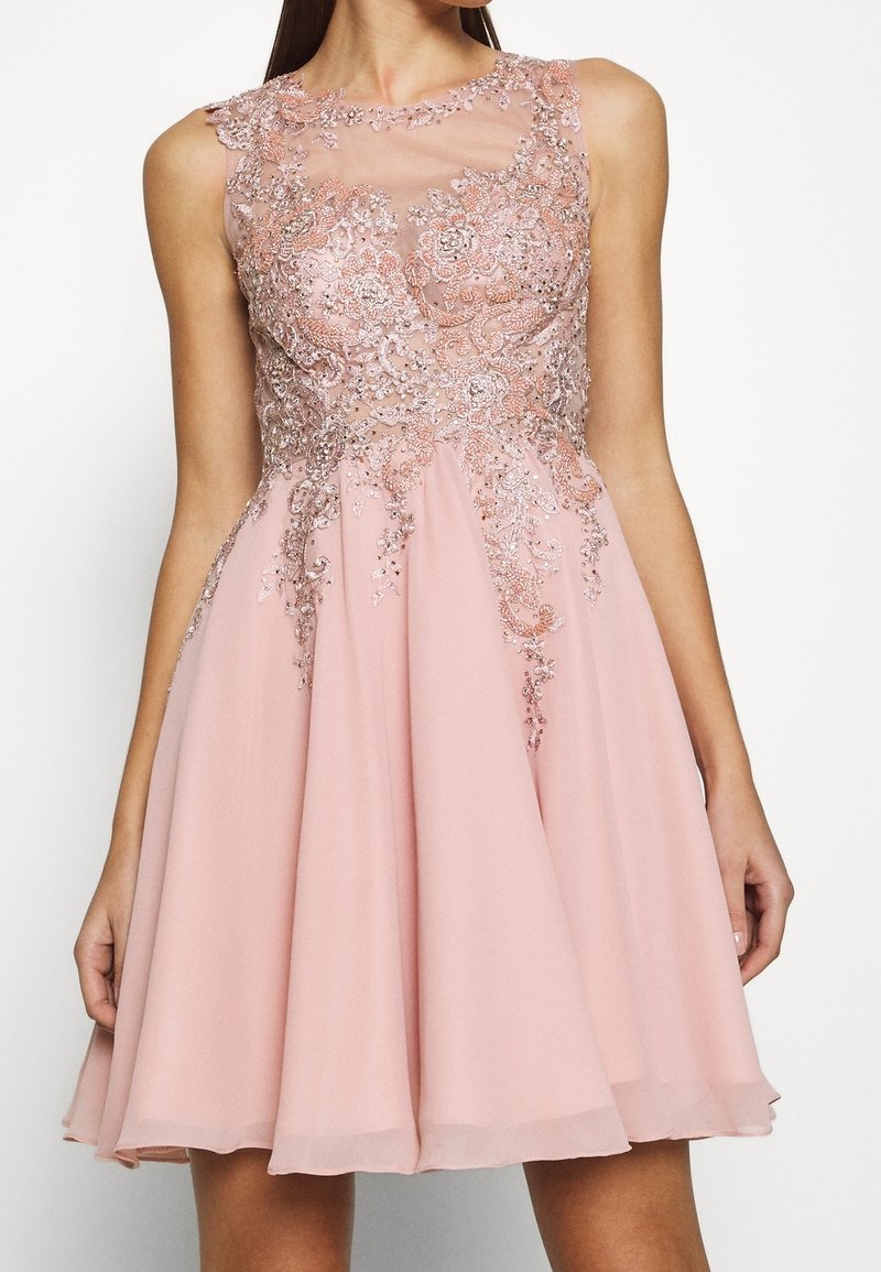Robe rose sans manches longueur genou avec dentelle florale complexe et ornements perles sur le corsage et l'encolure transparente.