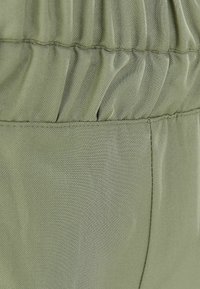 Zielony materiał o gładkiej fakturze ma marszczone elementy w talii oraz płaską powierzchnię, podkreślając swoją lekkość i elastyczność.