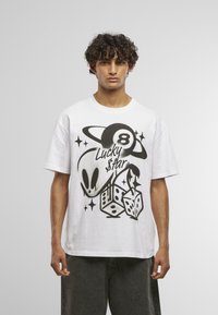 Hvid bomulds T-shirt med et sort grafisk design, der viser en alien, terninger og stjerner, og fremhæver teksten "Lucky $tar" samt tallet 8.