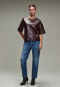 Burgundy faux crocodile leather top with wide short sleeves, paired with light blue straight-leg jeans and black ankle boots.