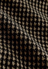 Tekstil med et hundetandsmønster i sort og beige. Blød, vævet tekstur med skiftevis mørke og lyse firkanter.