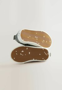 Sneakers met een grijze bovenkant, witte zool en een visgraatpatroon op de bruine rubberen zool. Bevat een lichte demping voor grip.
