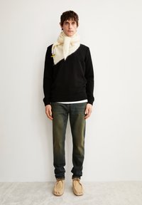 Zwarte trui met lange mouwen, lichte denim jeans, beige mokasins en een oversized crèmekleurige sjaal met een label. Minimalistisch ontwerp en neutrale kleuren.