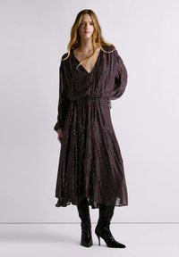 Vestido largo y fluido con escote en V profundo, cintura fruncida y mangas largas. Presenta una base burdeos con rayas verticales coloridas.